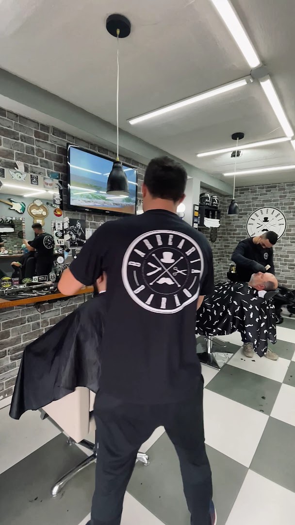 Barbeiro atendendo cliente na Barbearia Barão, com decoração de rock e piso xadrez