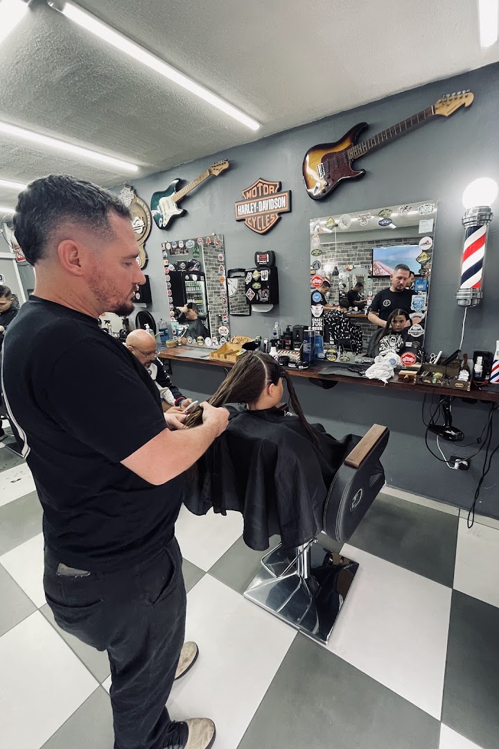 Barbeiro corta o cabelo comprido de uma criança na cadeira da barbearia, com decoração de rock ao fundo